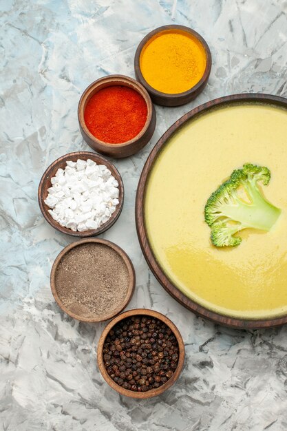 Vertikale Ansicht der cremigen Brokkolisuppe in einer braunen Schüssel und verschiedenen Gewürzen auf grauem Hintergrund