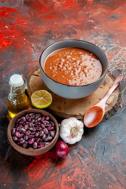 Vertikale Ansicht der Delikatessuppe zum Abendessen mit einem Löffel und einer Zitrone auf einem hölzernen Tablettbohnen-Knoblauchzwiebel und einer Ölflasche auf gemischtem Farbhintergrund