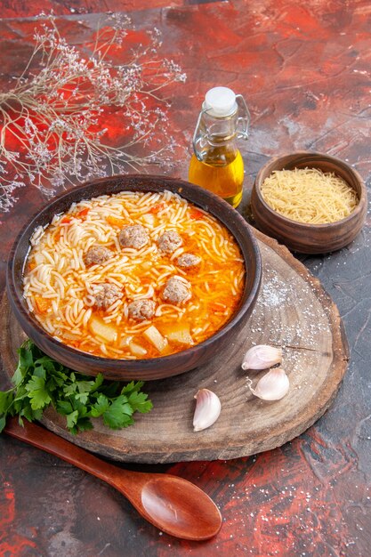 Vertikale Ansicht der leckeren Nudelsuppe mit Hühnchen auf Holzbrett Grüns Ölflasche Löffel Knoblauch auf dunklem Hintergrund