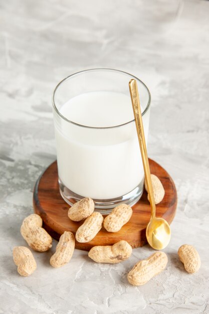 Vertikale Ansicht der mit Milch gefüllten Glasschale auf Holztablett und Trockenfrüchtelöffel auf weißem Hintergrund