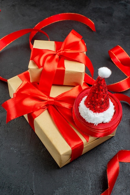 Vertikale Ansicht der schönen Geschenke mit rotem Band und Weihnachtsmannhut auf dunklem Tisch