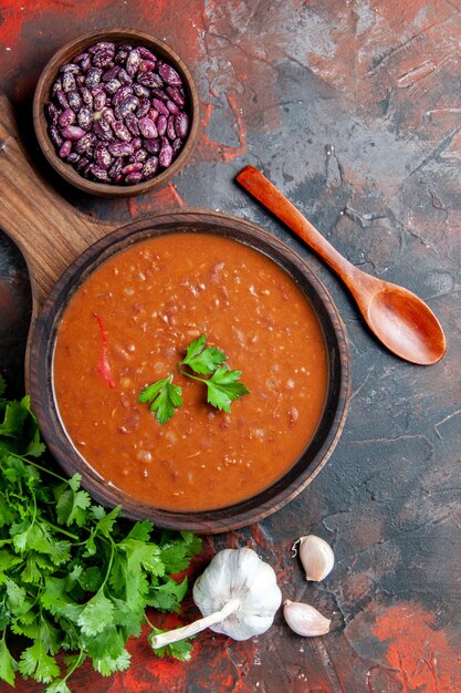 Vertikale Ansicht der Tomatensuppe auf einem braunen Schneidebrett auf einem gemischten Farbhintergrund