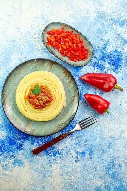 Vertikale Ansicht des Abendessens mit köstlichen Spagetti auf einer grauen Tellergabel ganz und gehacktem Pfeffer auf blauem Tisch