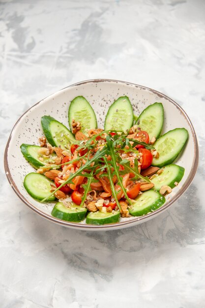 Vertikale Ansicht des hausgemachten gesunden köstlichen veganen Salats, der mit gehackten Gurken in einer Schüssel auf befleckter weißer Oberfläche verziert wird
