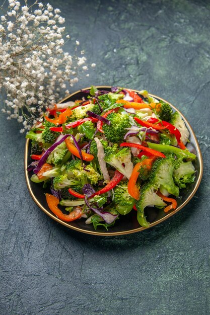 Vertikale Ansicht des köstlichen veganen Salats in einem Teller mit verschiedenem Gemüse und der weißen Blume der Gabel auf dunklem Hintergrund mit freiem Raum