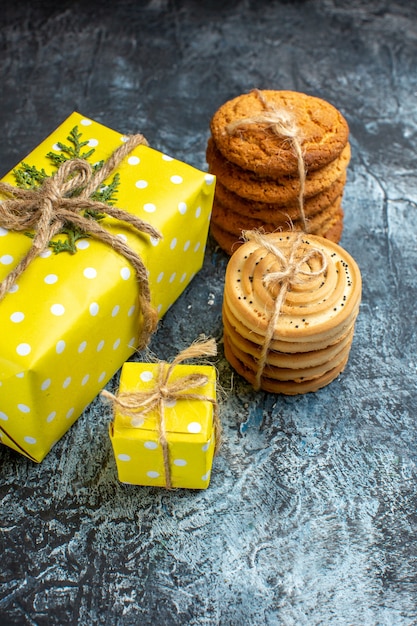 Vertikale Ansicht des Weihnachtshintergrundes mit schönen gelben Geschenkboxen und gestapelten Keksen auf dunklem Tisch