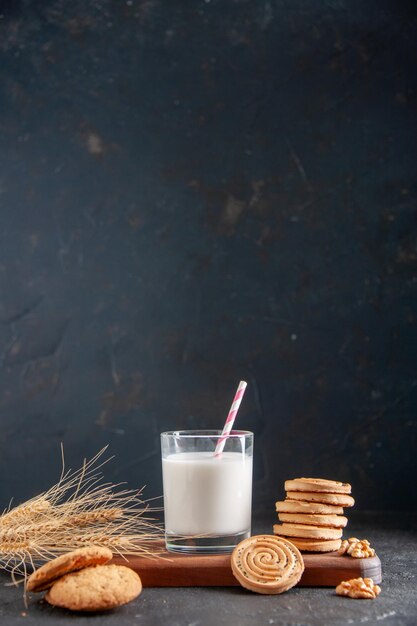 Vertikale Ansicht einer frischen Milch in einem Glas Kekse Spikes auf Holzbrett Walnüsse Erdnüsse auf dunklem Hintergrund
