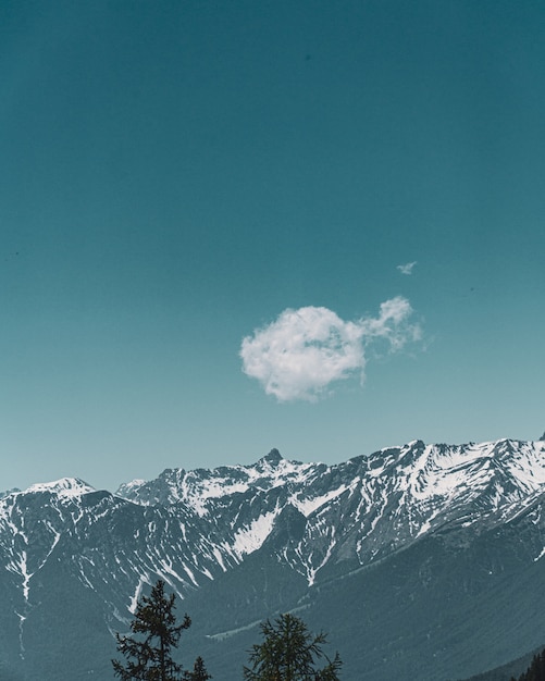 Vertikale Ansicht einer niedlichen kleinen Wolke mit dem Hintergrund der Berge und des blauen Himmels