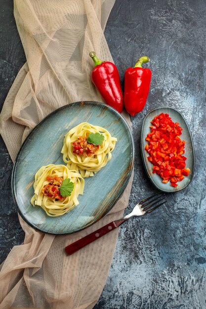 Vertikale Ansicht eines blauen Tellers mit köstlichen Pastagerichten, serviert mit Tomaten und Fleisch auf einem braunen Handtuch zum Abendessen seine Zutaten