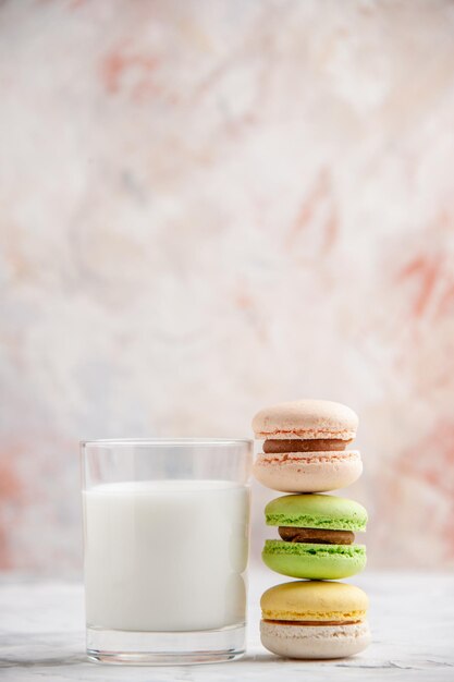 Vertikale Ansicht eines Glases Milch und bunter köstlicher Macarons auf pastellfarbenem Hintergrund mit freiem Platz