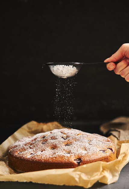 Vertikale Ansicht eines Kirschkuchens mit Zuckerpulver und Zutaten auf der Seite auf einem schwarzen Hintergrund