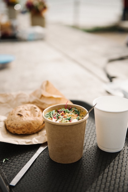 Vertikale Ansicht eines Tisches mit einer Tasse Kaffeesalat und Brot auf einem unscharfen Hintergrund