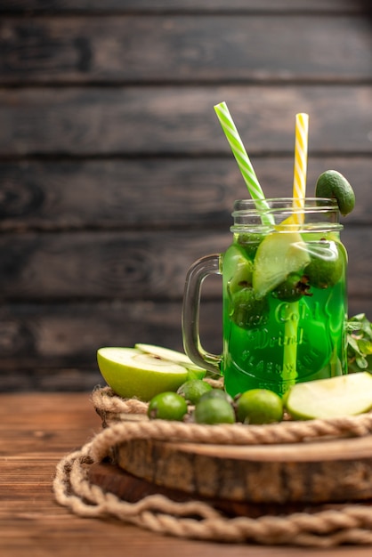 Vertikale Ansicht von frischem, köstlichem Fruchtsaft, serviert mit Apfel und Feijoas auf einem Holzbrett auf einem braunen Tisch