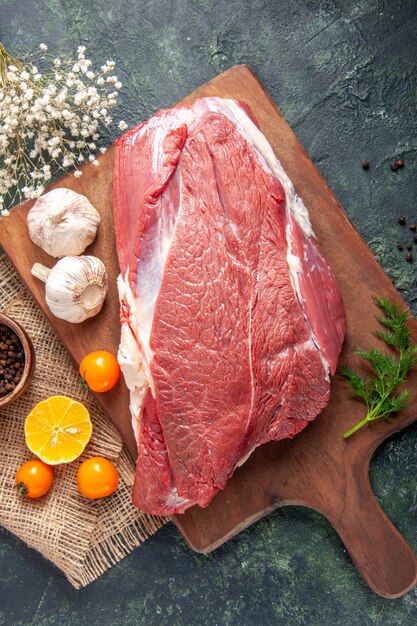 Vertikale Ansicht von frischem rohem rotem Fleisch, grünem Knoblauch auf braunem Holzbrett Tomatenpfeffer auf nacktem Handtuchmesser auf dunklem Hintergrund