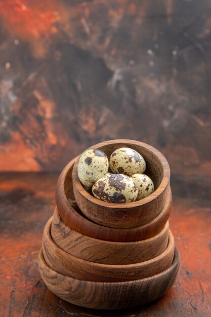 Vertikale Ansicht von frischen Eiern in gestapelten Holzschalen auf braunem Hintergrund