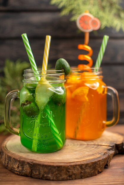 Vertikale Ansicht von frischen Fruchtsäften in einem Glas serviert mit Röhren auf einem Holzbrett auf einem braunen Tisch