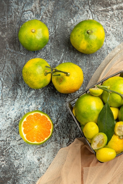 Kostenloses Foto vertikale ansicht von frischen kumquats und zitronen in einem schwarzen korb auf handtuch und vier zitronen auf grauem hintergrund