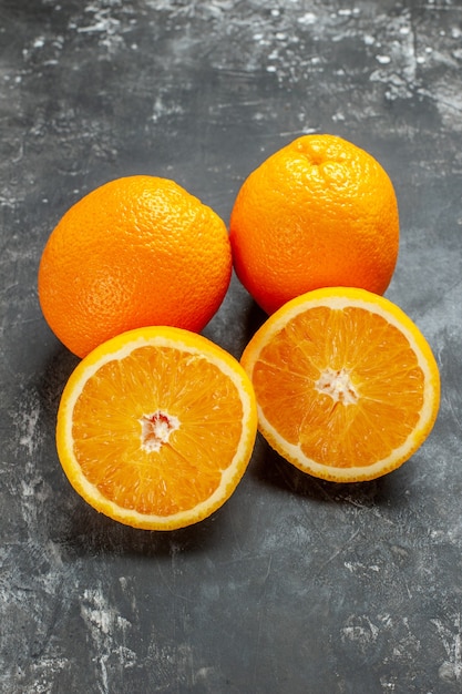 Vertikale Ansicht von ganzen und geschnittenen natürlichen organischen frischen Orangen, die in zwei Reihen auf dunklem Hintergrund aufgereiht sind
