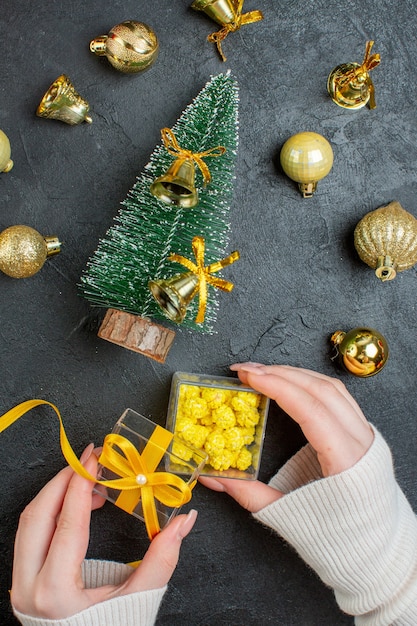 Vertikale Ansicht von Hand, die Geschenkboxen und Weihnachtsbaumdekorationszubehör auf dunklem Hintergrund hält