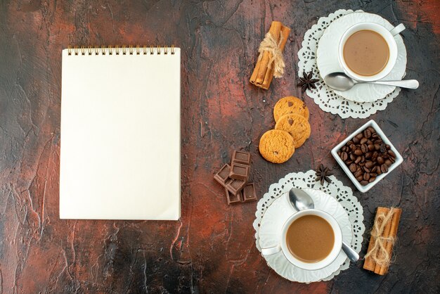 Vertikale Ansicht von köstlichem Kaffee in weißen Tassen Cookies Zimt-Limonen-Schokoriegel und Notizbuch auf gemischtem Farbhintergrund