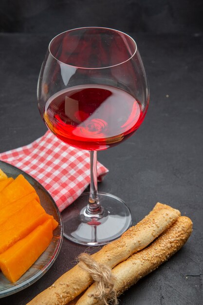 Vertikale Ansicht von köstlichem Rotwein in einem Glasbecher und geschnittenem Käse auf einem roten, abgestreiften Handtuch auf einem schwarzen Tisch