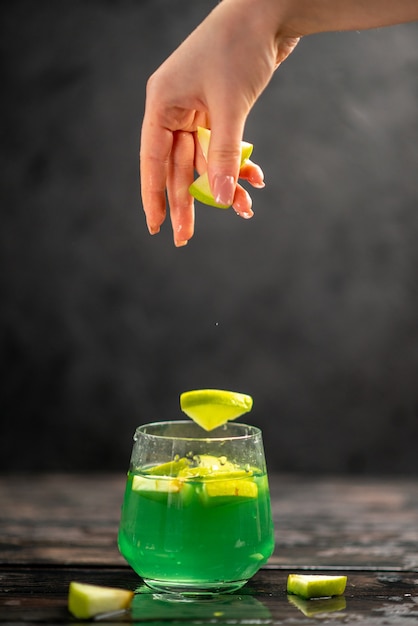 Vertikale ansicht von köstlichem saft in einer glashand, die apfellimetten auf dunklem hintergrund einsetzt