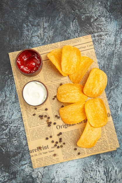Kostenloses Foto vertikale ansicht von köstlichen hausgemachten chips und pfefferschüssel mayonnaise ketchup und soße auf zeitung auf grauem tisch