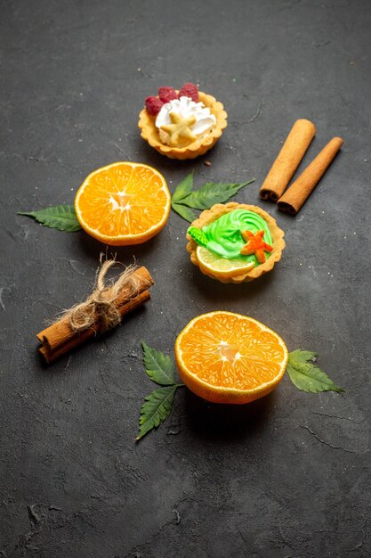 Vertikale Ansicht von leckeren Keksen, Zimtlimetten und halbgeschnittenen Orangen mit Blättern auf dunklem Hintergrund