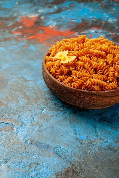 Vertikale Ansicht von roher italienischer Pasta in einer braunen Schüssel auf blauem Tisch