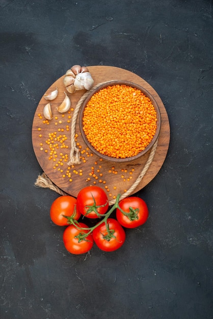 Vertikale Ansicht von roten Linsenseilknoblauch auf hölzernen runden Bretttomaten mit Stielen auf schwarzem Hintergrund