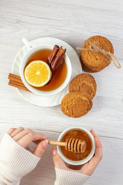 Vertikale Ansicht von schwarzem Tee mit Zitrone und Zimtlimetten gestapelt Kekse Honig auf weißem Hintergrund