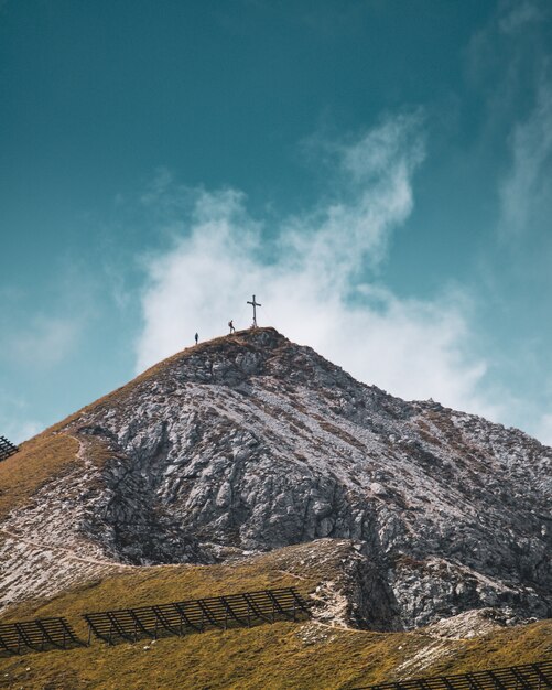 Vertikale Ansicht von zwei Personen, die nahe dem Kreuz auf der Spitze eines Gipfels klettern