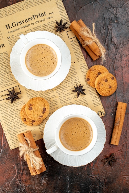 Kostenloses Foto vertikale ansicht von zwei tassen kaffeeplätzchen-zimt-limonen auf einer alten zeitung auf dunklem hintergrund