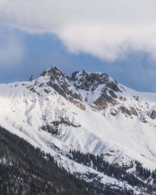 Vertikale Aufnahme der schneebedeckten Gipfel der Berge unter dem bewölkten Himmel