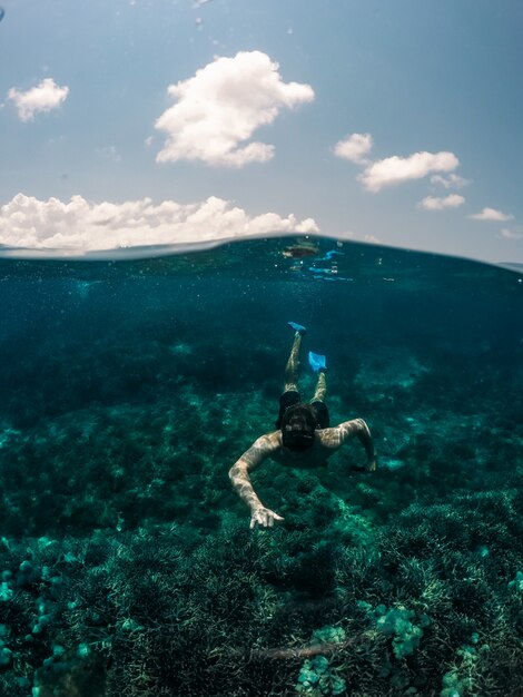 Vertikale Aufnahme des Mannes, der unter Wasser mit dem Himmel im Hintergrund schwimmt