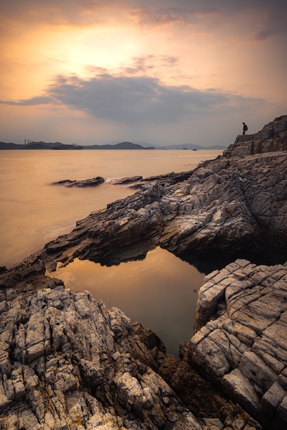 Vertikale Aufnahme des Wassers und der Klippen während eines Sonnenuntergangs an einem bewölkten Himmel