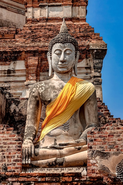 Vertikale Aufnahme einer alten Buddha-Statue, die mit gelbem und orangefarbenem Stoff bedeckt ist