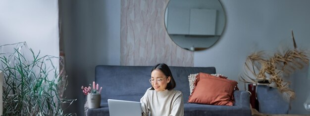 Kostenloses Foto vertikale aufnahme einer berufstätigen koreanerin, die zu hause mit laptop auf dem boden sitzt und am computer lernt