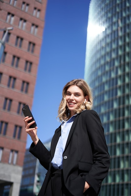 Vertikale Aufnahme einer erfolgreichen Geschäftsfrau im Anzug, die auf ihrem Weg t ein Smartphone mit einem Mobiltelefon hält