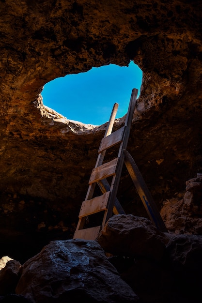 Vertikale aufnahme einer felsigen höhle mit einem großen loch und einer holzleiter - perfekt für das alte minenkonzept Premium Fotos