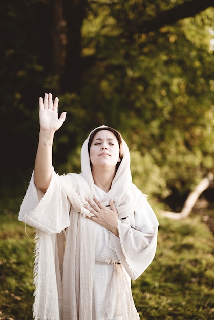 Vertikale Aufnahme einer Frau, die ein biblisches Gewand mit ihren Händen zum Himmel betend trägt