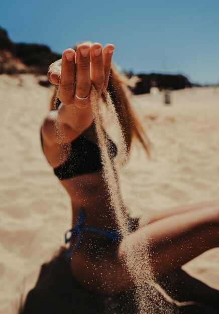 Vertikale Aufnahme einer Frau im Bikini, die mit Sand am Strand posiert