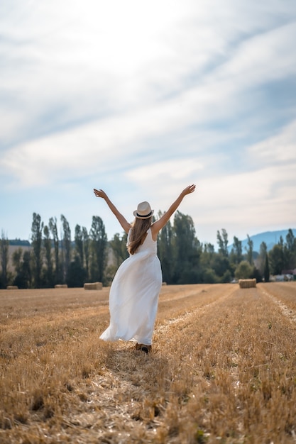 Vertikale Aufnahme einer fröhlichen Frau in einem weißen Kleid, die unter dem Sonnenlicht durch ein Feld läuft