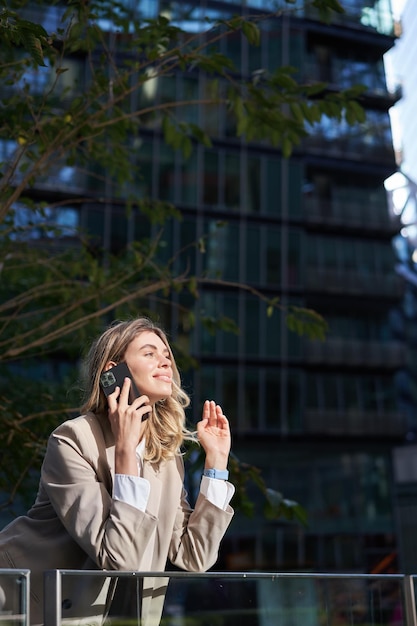 Vertikale Aufnahme einer Geschäftsfrau bei einem Anruf, die außerhalb des Business Centers steht und mit dem Handy telefoniert