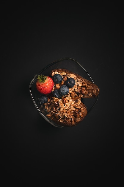 Vertikale Aufnahme einer Glasschale eines gesunden Snacks mit Blaubeeren, Erdbeere auf einem schwarzen Tisch