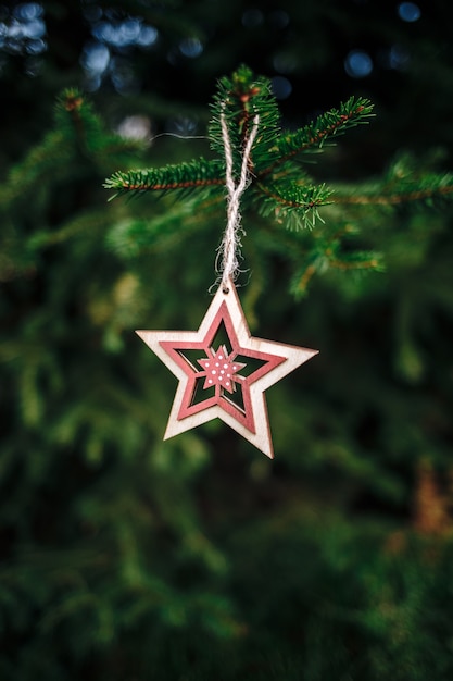 Vertikale Aufnahme einer hölzernen sternförmigen Weihnachtsverzierung, die von einer Kiefer hängt