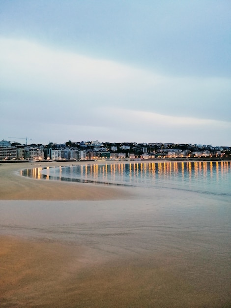 Vertikale Aufnahme einer hypnotisierenden Abendlandschaft von Stadtlichtern, die im Ozean reflektieren