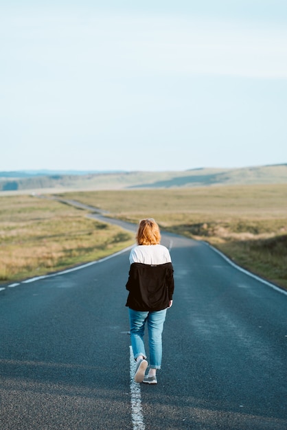 Vertikale Aufnahme einer jungen Frau in Jeans, die auf der Autobahn geht