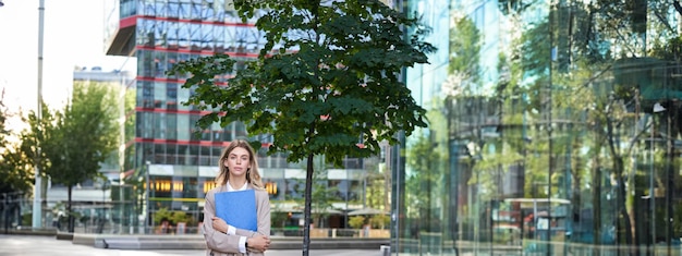 Kostenloses Foto vertikale aufnahme einer jungen geschäftsfrau im beigen anzug, die dokumente in den händen hält und selbstbewusst blickt