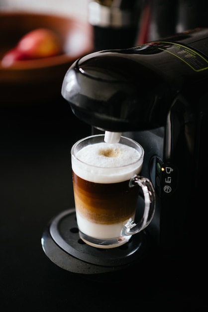 Vertikale Aufnahme einer Kaffeemaschine, die ein Nescafe in einem Glas macht